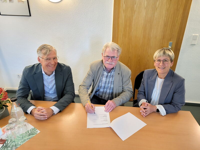 drei Personen an Tisch, in der Mitte ein Vertrag