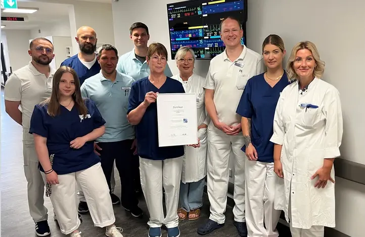 Gruppenbild: 10 Personen, in der Mitte hält eine Frau das Zertifikat in die Kamera