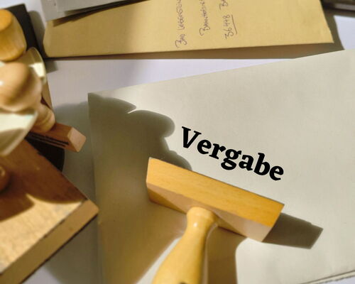 Schreibtisch mit Briefumschlägen und Stempel, Schriftzug Vergabe