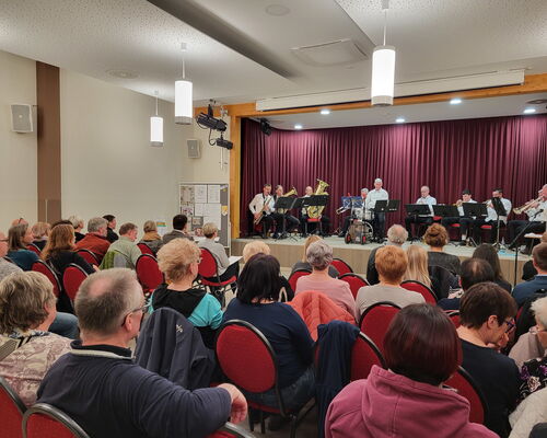 Saal mit Stuhlreihen und Menschen, auf der Bühne die Steinbacher Trachtenkapelle