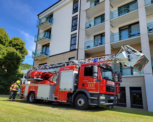 Feuerwehrauto mit Drehleiter steht auf Wiese vor mehrstöckigen Klinikgebäude