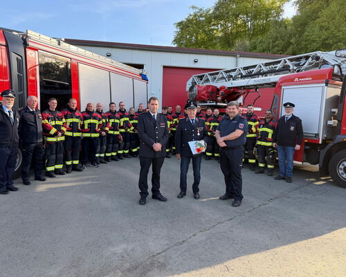 Feuerwehleute in Einsatzkleidung stehen Spalier für alten Kameraden, der Urkunde hält und Orden an Ausgehuniform trägt