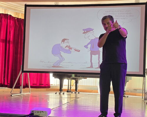 Muhsin Omurca steht auf der Bühne, im Hintergrund Leinwand mit Cartoon
