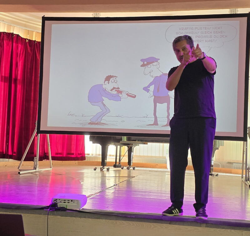 Muhsin Omurca steht auf der Bühne, im Hintergrund Leinwand mit Cartoon