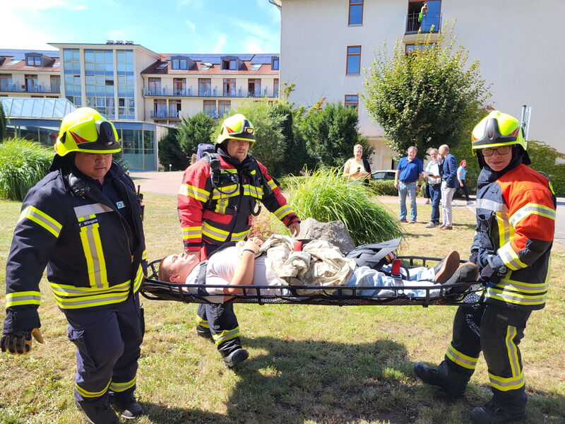 eine scheinbar verletzte Person wird von drei Feuerwehrleuten auf einer Trage transportiert