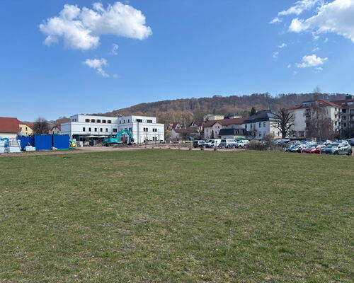 Wiesenfläche, im Hintergrund eine Baustelle, Parkplätze und Gebäude