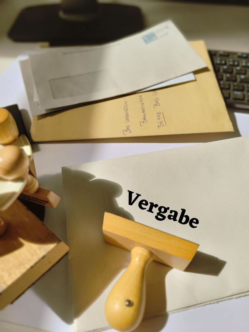 Schreibtisch mit Briefumschlägen und Stempel, Schriftzug Vergabe