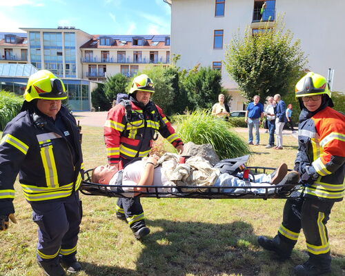eine scheinbar verletzte Person wird von drei Feuerwehrleuten auf einer Trage transportiert