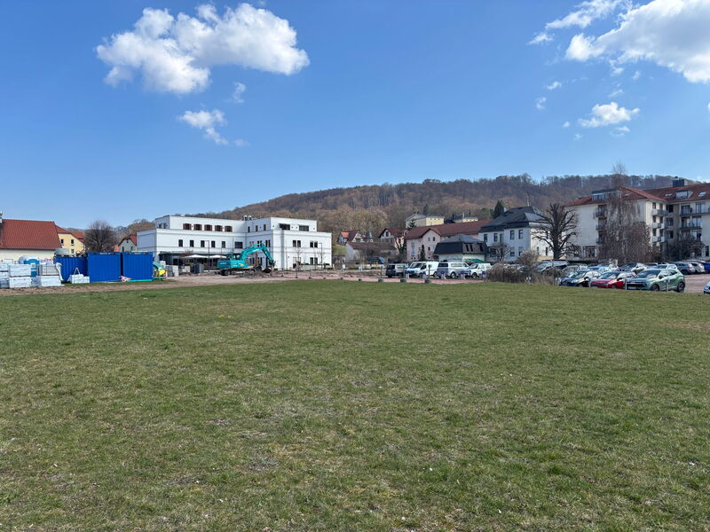 Wiesenfläche, im Hintergrund eine Baustelle, Parkplätze und Gebäude