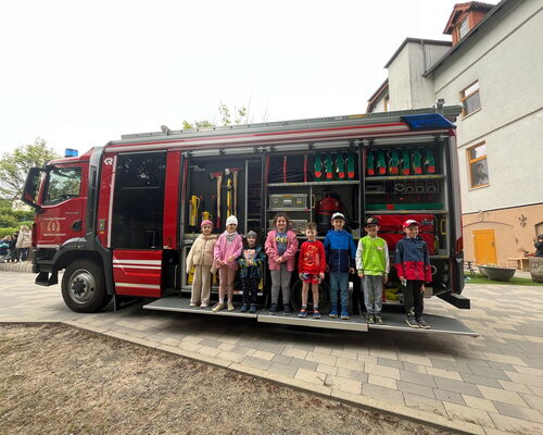 Kindergartenkinder stehen auf ausgefahrener Rampe an einem Feuerwehrfahrzeug