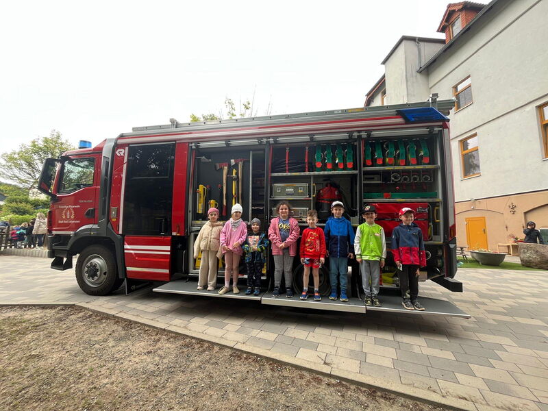 Kindergartenkinder stehen auf ausgefahrener Rampe an einem Feuerwehrfahrzeug