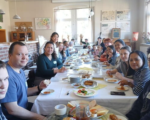 Zahlreiche Menschen unterschiedlicher Nationalität sitzen an einer langen Tafel und essen