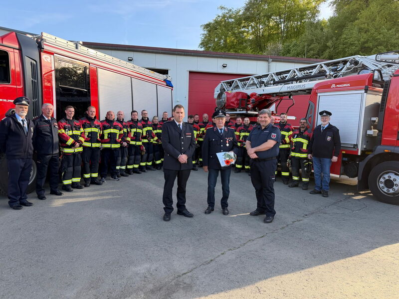 Feuerwehleute in Einsatzkleidung stehen Spalier für alten Kameraden, der Urkunde hält und Orden an Ausgehuniform trägt