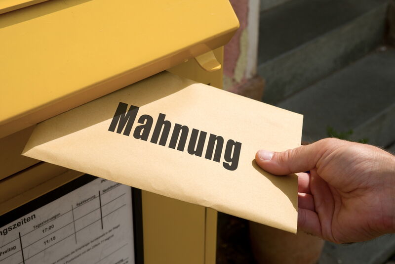 Hand steckt Brief mit Aufschrift MAhnung in Postbriefkasten