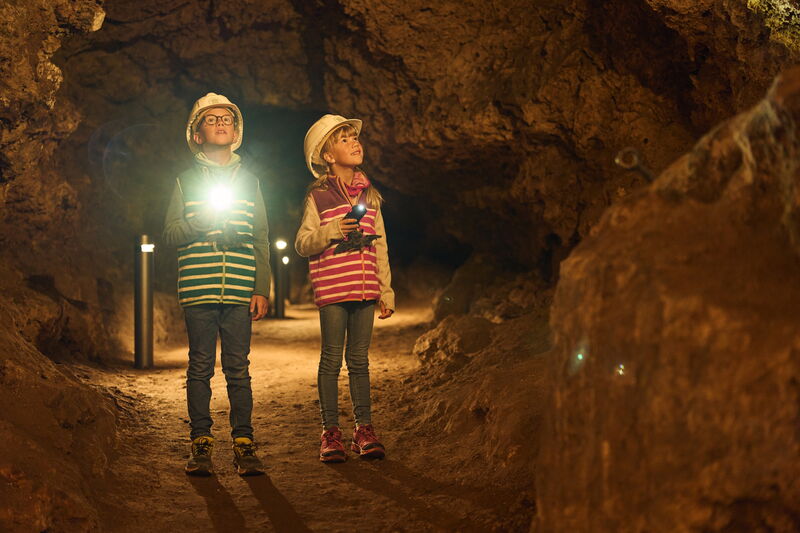 zwei Kinder mit Taschenlampe und Helm stehen in einer Höhle