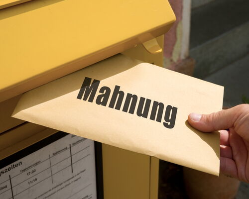 Hand steckt Brief mit Aufschrift MAhnung in Postbriefkasten