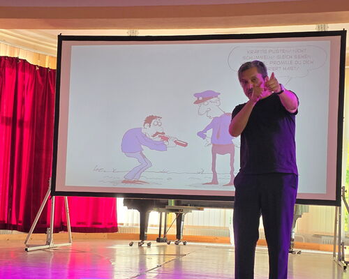 Muhsin Omurca steht auf der Bühne, im Hintergrund Leinwand mit Cartoon