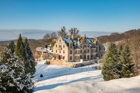 Schloss im Schnee vor blauen Himmel, umgeben von Berg- und Parklandschaft