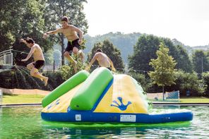 zwei Jungen und 1 Mann springen von aufblasbarer Schwimminsel ins Wasser