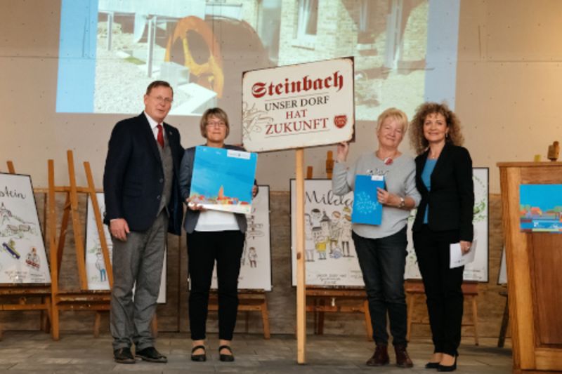 Links Ministerpräsident Bodo Ramelow, rechts Ministerin Birgit Keller, überreichen Sonderpreis an Susanne Rakowski und Elvira Schmager (in der Mitte vom Bild), im Hintergrund ist ein Bild vom Wasserrad auf die Wand projiziert