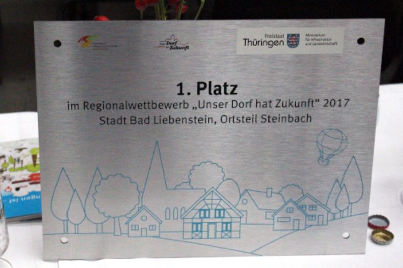 Siegerplakette zeigt Wettbewerbslogo und Aufscchirft: 1. Platz im Regionalwettbewerb "Unser Dorf hat Zukunft" 2017, Stadt Bad Liebenstein Ortsteil Steinbach