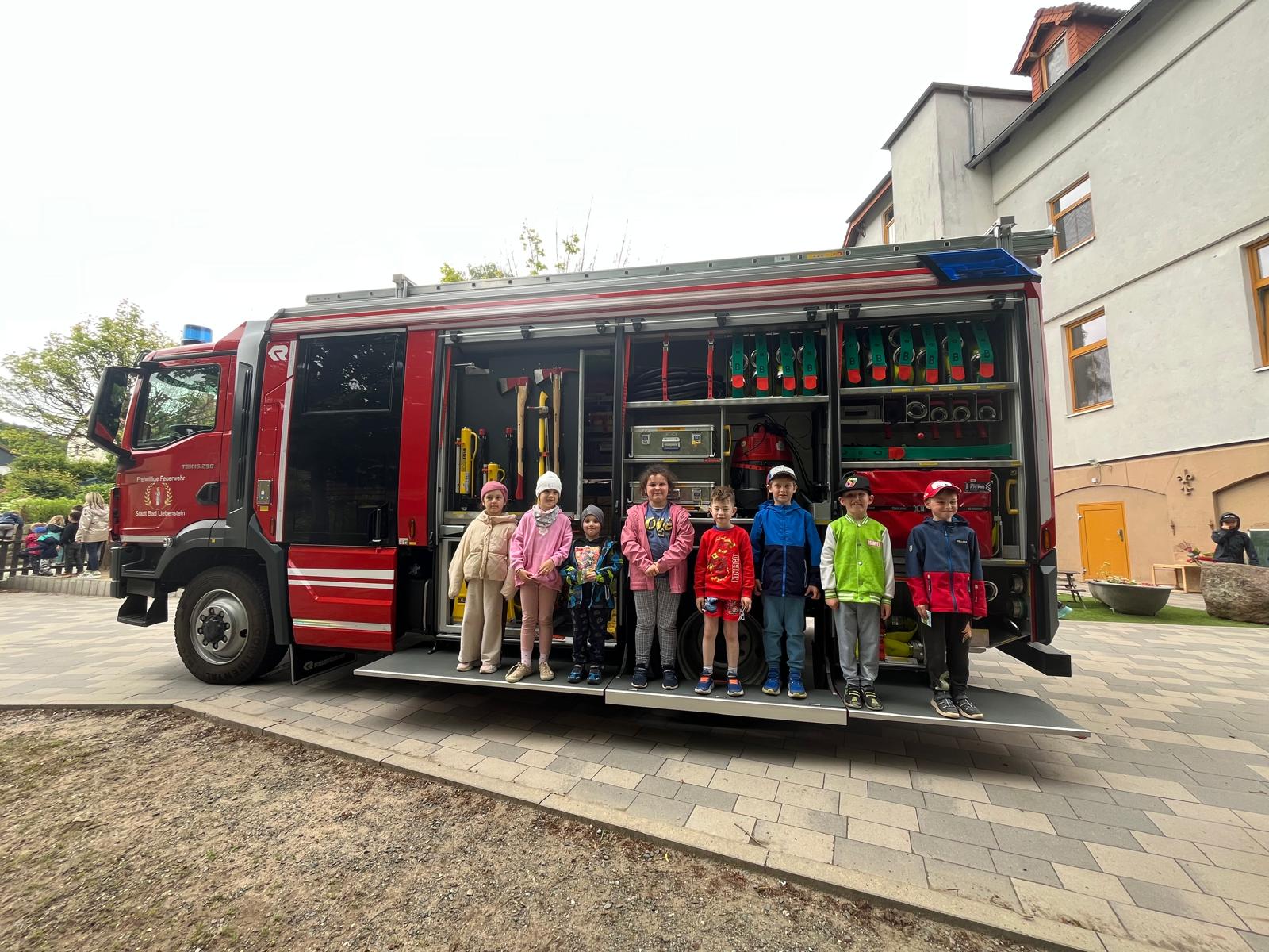 Kindergartenkinder stehen auf ausgefahrener Rampe an einem Feuerwehrfahrzeug