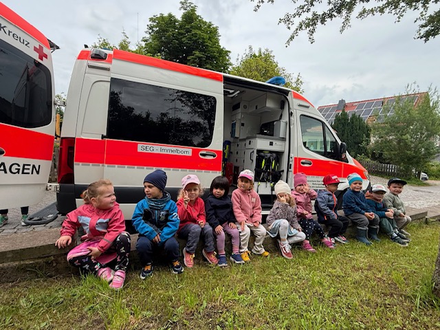Ein Dutzend Kindergartenkinder sitzt vor einem Rettungswagen