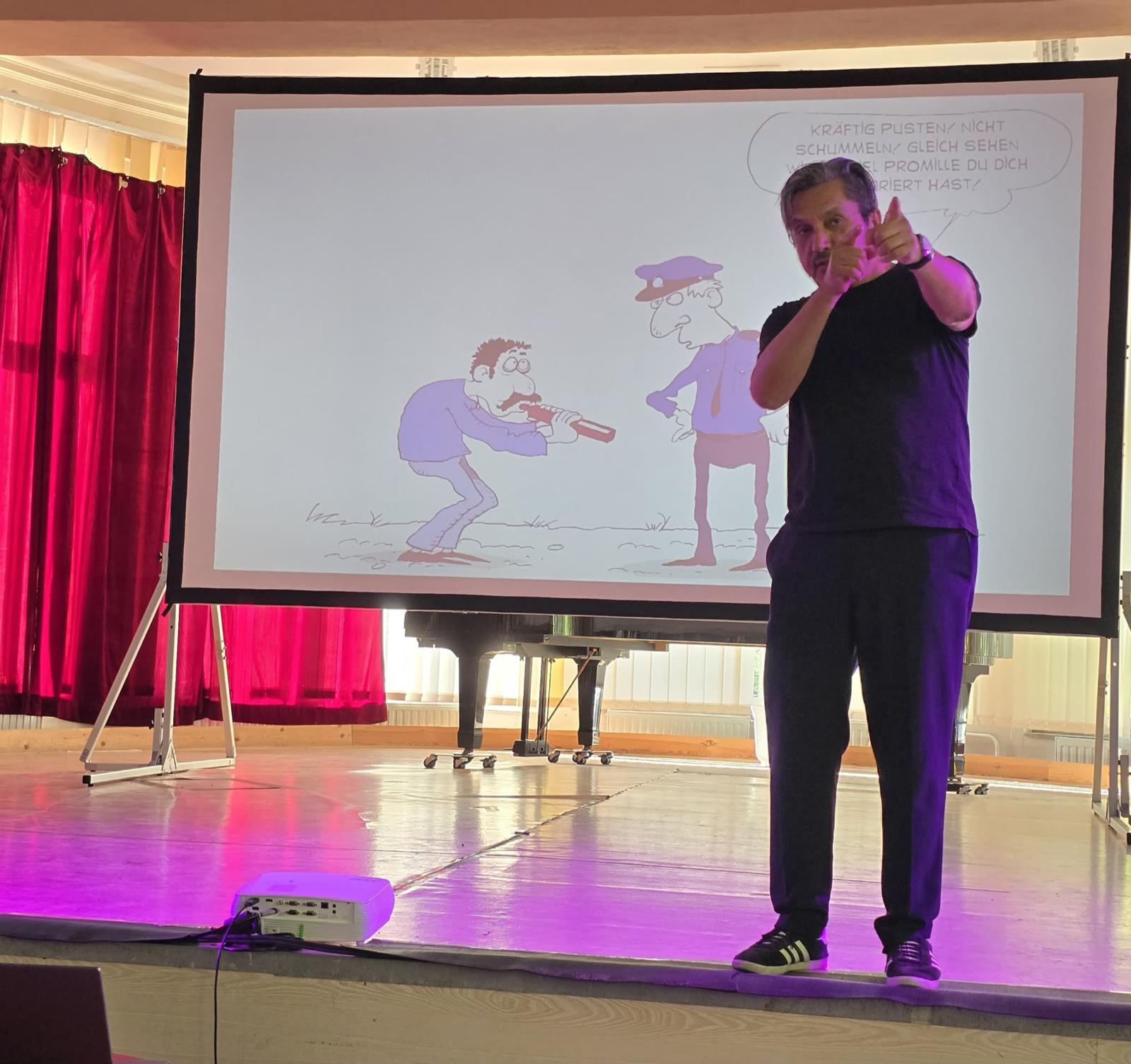 Muhsin Omurca steht auf der Bühne, im Hintergrund Leinwand mit Cartoon
