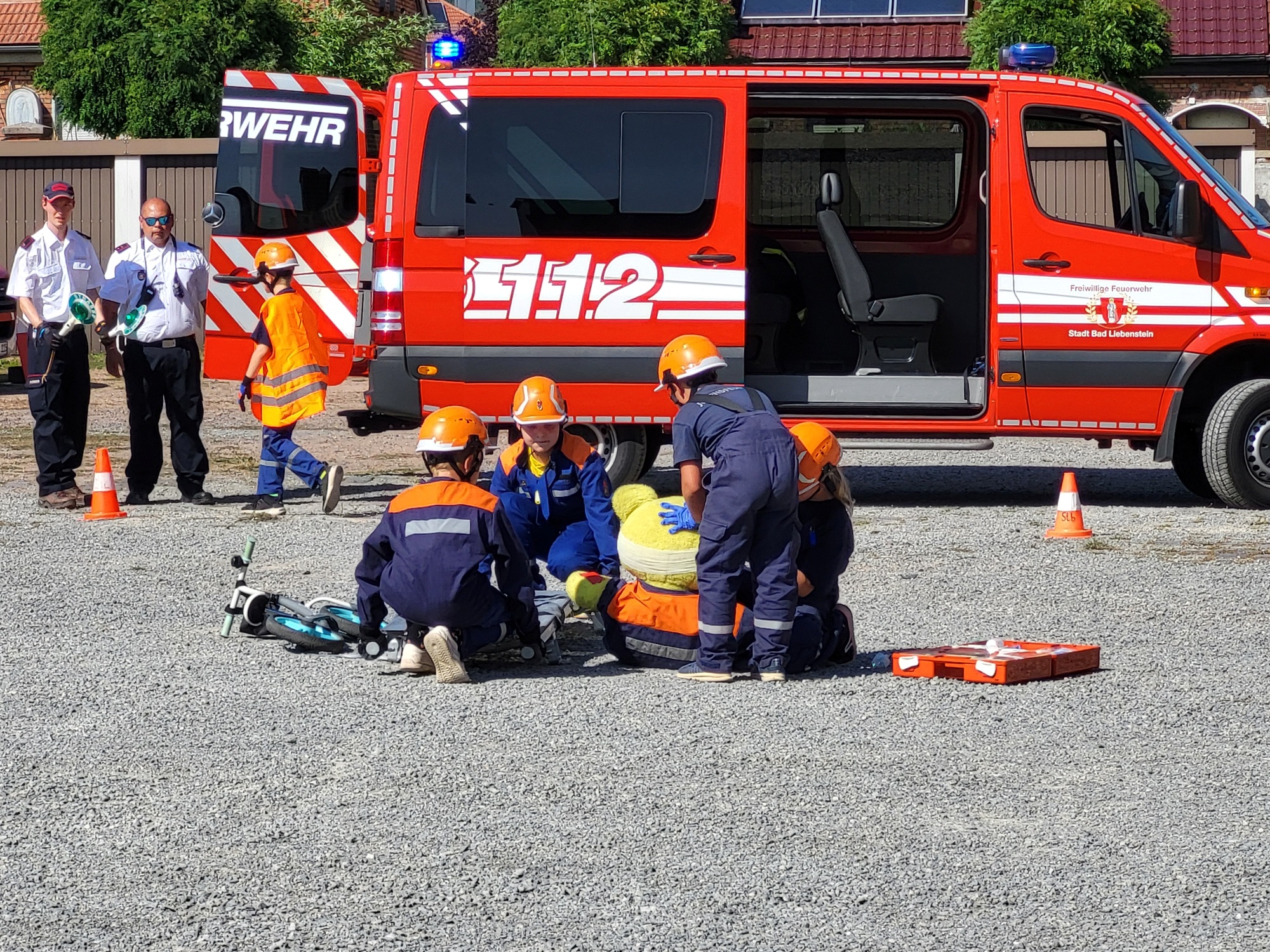 Kinder der Jugendfeuerwehr versorgen einen riesengroßen Teddy nach einem Fahrradunfall